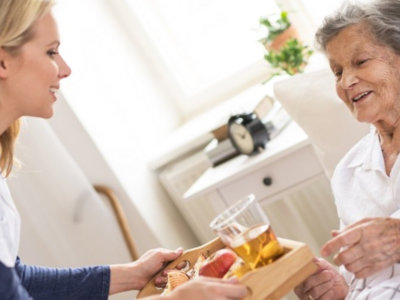 caregiver seving food to an elder woman on bed